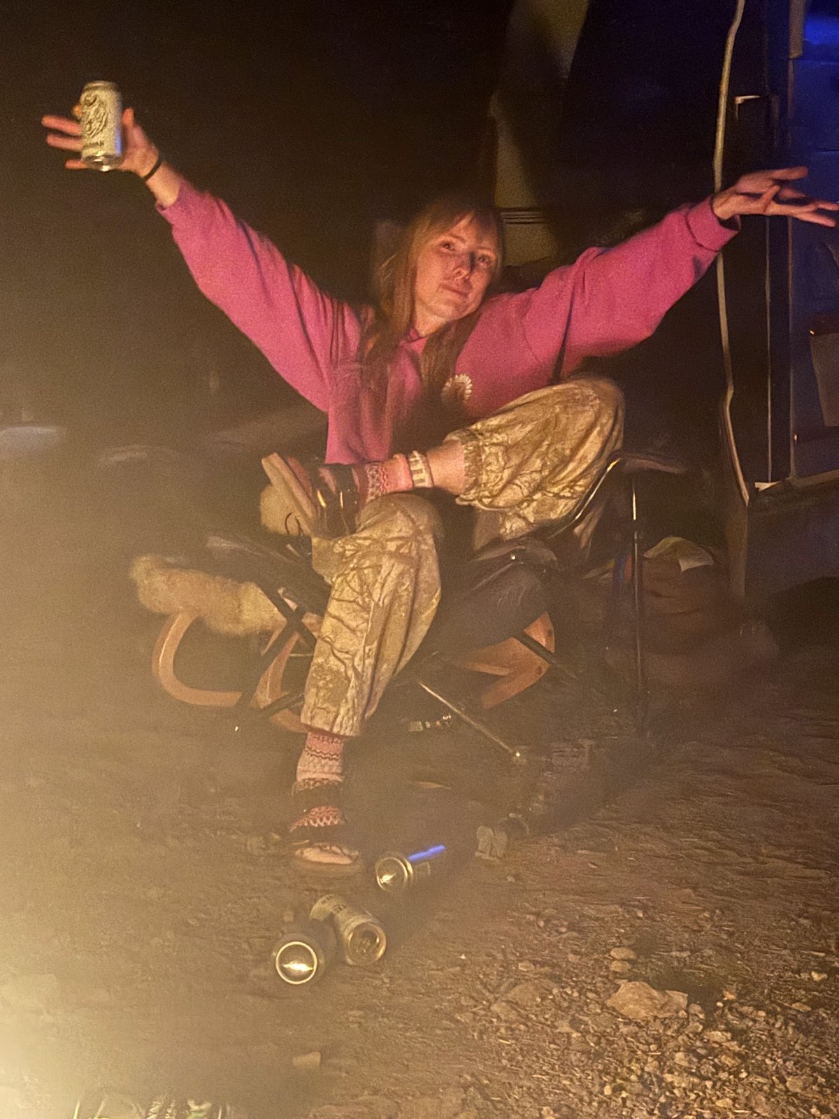 A crew member in a pink top beside the campfire with arms outstretched